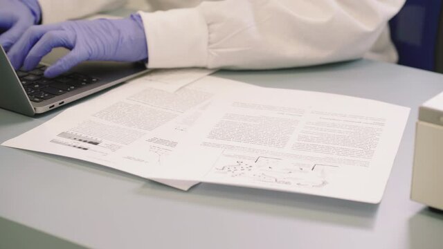 Woman Researching Pattern Analysis In Biotechnology Laboratory With Laptop And Papers On Table. - crop shot