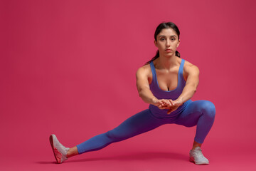 Young woman performing bodyweight side lunges on maroon background