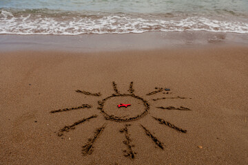 symbol of the sun and a plane by the sea. Painted sun on the sand, sea coast, figure of a red plane, sea waves