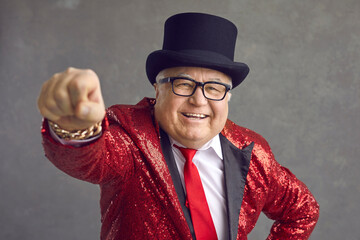 Funny rich mature man in eyeglasses, bling fancy sequin jacket and black top hat smiling and...