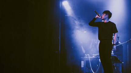 Singer holding a microphone stand and performing on stage. Rock concert show set up.