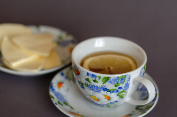 Cup of tea with lemon and Saucer with sliced cheese on gray background.