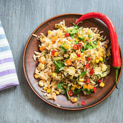 Spicy fried rice with vegetables on a plate with a pod of hot pepper - an oriental vegetarian lunch.