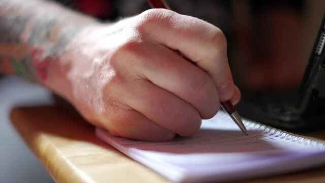 Caucasian man with tattooed arm crossing chore task off ToDo list checkbox, dropping pen on pad of paper, working from home during Covid-19 Pandemic Quarantine. In 4k slot motion, shot on Sony A7Siii.