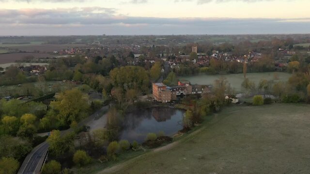 An aerial flight over Dedham Mill towards Dedham village at sunrise with low mist.