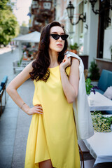 Young fashion girl on the street with style wearing a white jacket stylish draped over her shoulders. Attractive model walking at sunset along the streets of the city. Vertical photo.