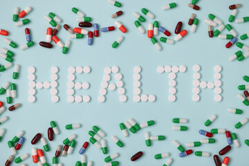 Word health is laid out from white pills on background of multicolored capsules closeup background