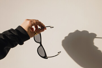 Female hand holding sunglasses over the white wall. Natural sunlight