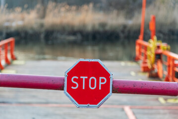 STOP sign and barrier before entering the river ferry. Late winter afternoon and snow is still visible on the bank