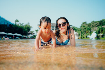 Fototapeta premium Asian mother and little son enjoying swimming in a swimming pool in summer vacation.