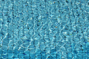 View through clean water to bottom of swimming pool lined with blue tiles