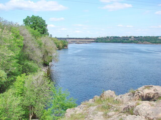 Fototapeta premium Walk on a narrow path on top of the Dnieper bank on the background of a dam under white clouds on the horizon.