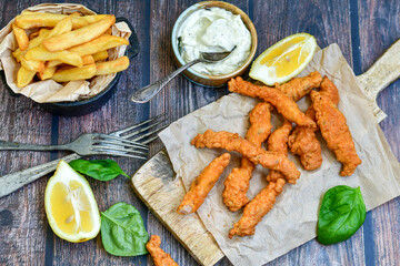 
 Crispy  deep fried   chicken strips  with sesame seeds and french fries . Breaded  with cornflakes chicken  breast fillets  with chilly peppers and fresh   basil on wooden rustic background