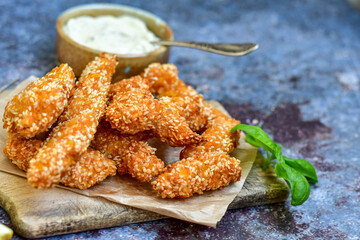 
 Crispy  deep fried   chicken strips  with sesame seeds and french fries . Breaded  with cornflakes chicken  breast fillets  with chilly peppers and fresh   basil on wooden rustic background