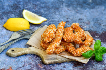 
 Crispy  deep fried home made    chicken strips Breaded  with  almond flour chicken  breast fillets  with chilly peppers and fresh   basil on wooden rustic background. Ketogenic diet food