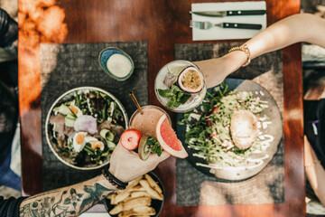 People toasting with different alcoholic beverages on top of a table filled with culinary food in restaurant