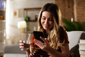 Beautiful young girl using the phone while drinkinng water. Portrait of smiling girl typing a message.