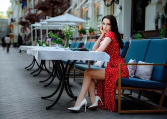 Cheerful pretty young lady in trendy clothes posing to the camera on the terrace in cafe. Lifestyle and Holiday activity. Dinner at the restaurant with a plate of salad and a glass of champagne.