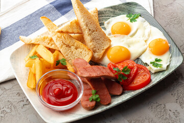 English breakfast with eggs, sausages, french toasts and potato wedges on gray table