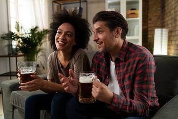 Boyfriend and girlfriend drinking beer at home. Happy couple watching sports game on tv..