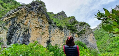 woman on a mountain path admires the trees growing on the rock of the steep slopes