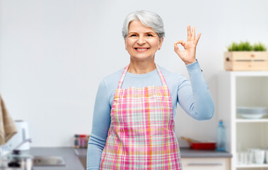 cooking, culinary and old people concept - portrait of smiling senior woman in apron showing ok...
