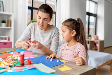 family, art and craft concept - mother spending time with her little daughter with glue making applique of color paper at home