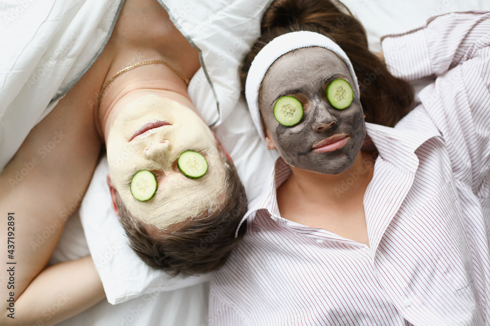 Wall mural man and woman apply clay mask for rejuvenation on face and cucumbers on eyes