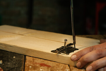 Carpenter screwing metal chrome hinges on wooden plank in the workshop.