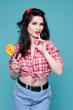 Pin up brunette girl with  black hair and wide smile holding finger to her mouth and lollipop in another hand. Copy space. Close up. English lessons and courses. 
