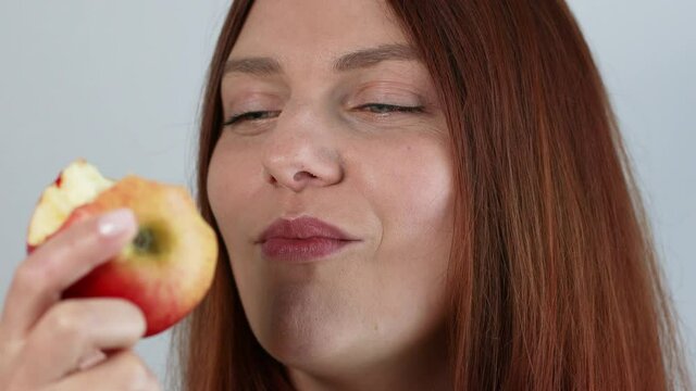 Young caucasian woman eating ripe red apple with closed eyes, enjoying fresh organic snack, healthy eating and lifestyle concept
