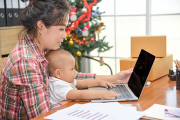 Pretty young single mom working at home on a laptop computer while holding her baby girl sitting on her lap enjoying playing computer.