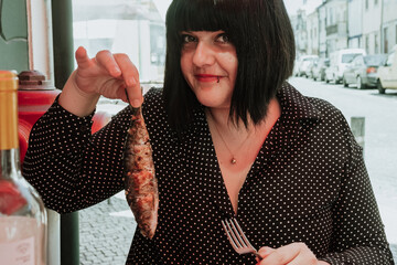 A young woman dressed in black with black hair and red lips holding a sardine in a restaurant in...