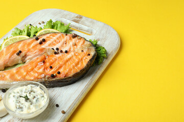 Concept of tasty eating with grilled salmon on yellow background