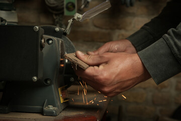 Handyman sharpening iron tool on electrical grinder stone