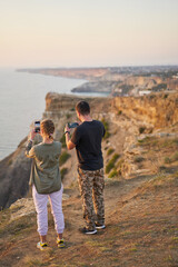 Couple is staying on the rock, taking photo and enjoying the sea view and the fresh air.