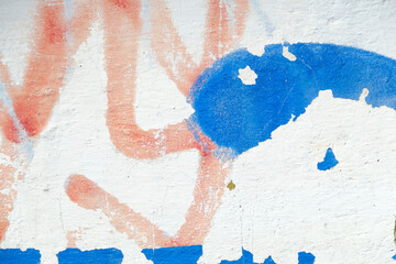 Weathered cement wall painted with peeled blue paint and red spray traces. Abstract vintage background. 