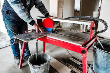 A worker is cutting a ceramic tile on a wet cutter saw machine.