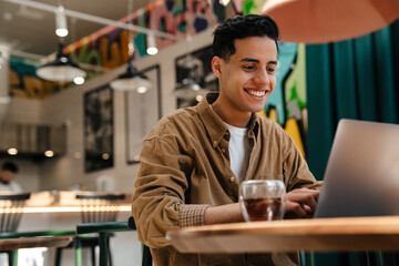Young hispanic man student sitting at the cafe table indoors - obrazy, fototapety, plakaty