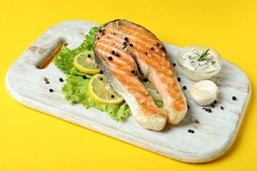 Concept of tasty eating with grilled salmon on yellow background