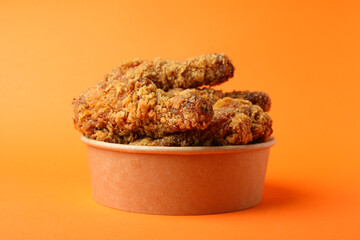 Bucket with fried chicken on orange background