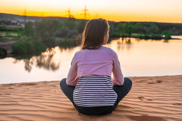 Little girl child sitting in yoga pose at sunset in front of the lake, the concept of relaxation and mental health