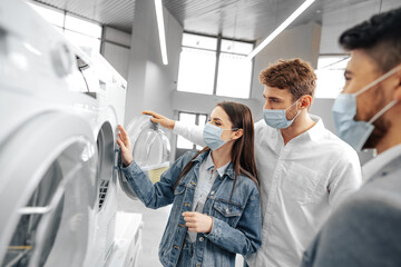 Salesman in hypermarket wearing medical mask demonstrates his clients a new washing machine