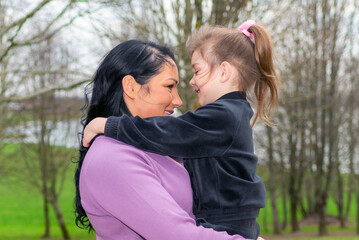 Fototapeta premium Beautiful mother and daughter play hugs in a spring park nature in profile looking at each other.
