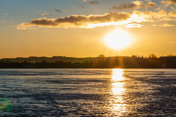 Winter landscape with frozen lake at sunrise or sunset. Lake glistening ice reflect a sun.Forest in the background.