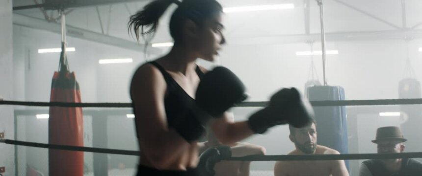 HANDHELD Spectators gather around ring to watch boxing sparring match between male and female fighters inside a gym. Shot with 2x anamorphic lens