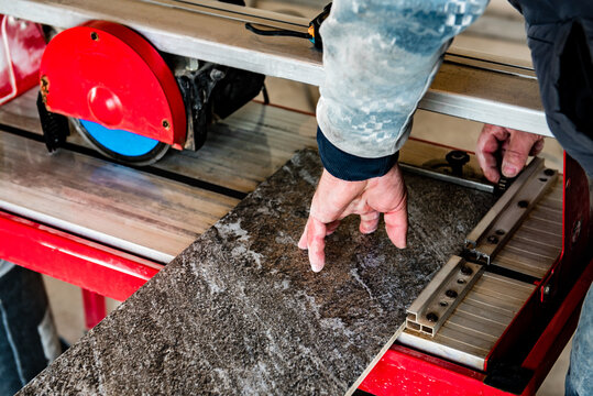 A worker is cutting a ceramic tile on a wet cutter saw machine.