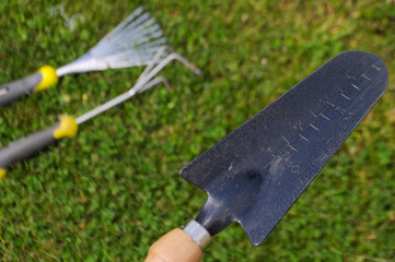Gardening equipment on a grass green background. Focus on a metal trowel 