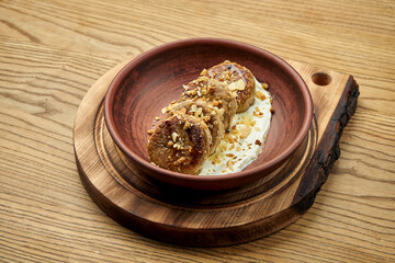 Delicious vegetarian tofu and banana cheese pancakes, with white sauce and nuts in a clay plate on a wooden background