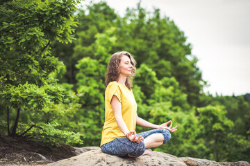 woman meditating in lotus pose on a rock in summer